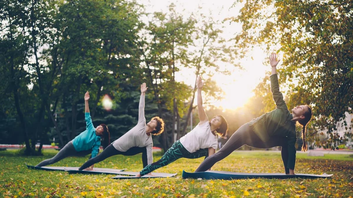 Four people holding a side-angle yoga pose on mats in a park at golden hour